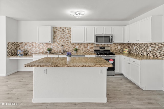 kitchen featuring white cabinetry, a center island, light stone counters, and appliances with stainless steel finishes