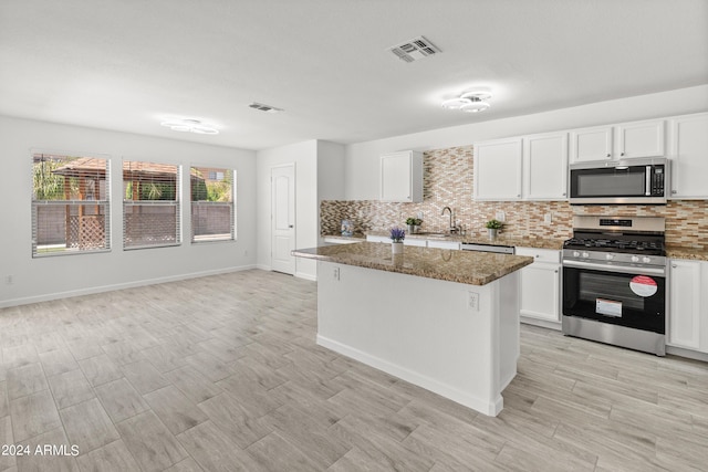 kitchen featuring appliances with stainless steel finishes, dark stone counters, sink, white cabinets, and a center island