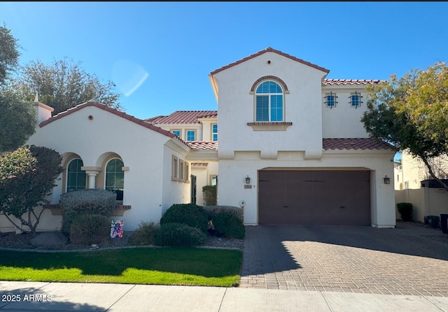 mediterranean / spanish-style home with a tile roof, decorative driveway, an attached garage, and stucco siding