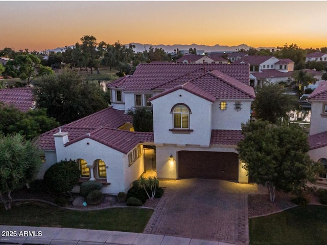 mediterranean / spanish home featuring stucco siding, a garage, a tiled roof, decorative driveway, and a residential view