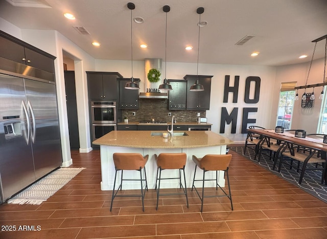 kitchen with visible vents, appliances with stainless steel finishes, wall chimney exhaust hood, and decorative backsplash