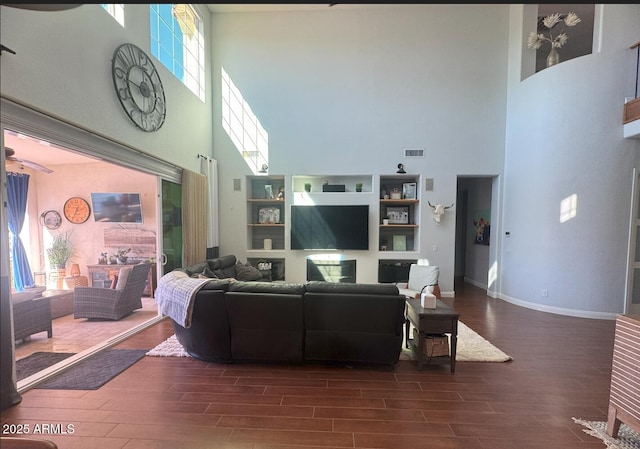 living area with visible vents, a towering ceiling, baseboards, and dark wood-style flooring