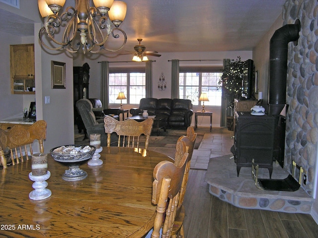 dining space with hardwood / wood-style flooring, a wood stove, and ceiling fan with notable chandelier