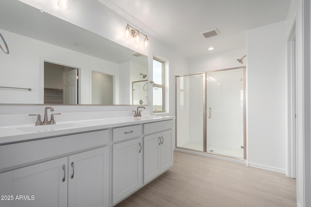 bathroom with a sink, double vanity, a shower stall, and visible vents