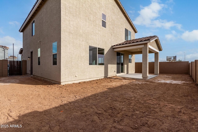 rear view of property with a patio, a fenced backyard, a tiled roof, a gate, and stucco siding