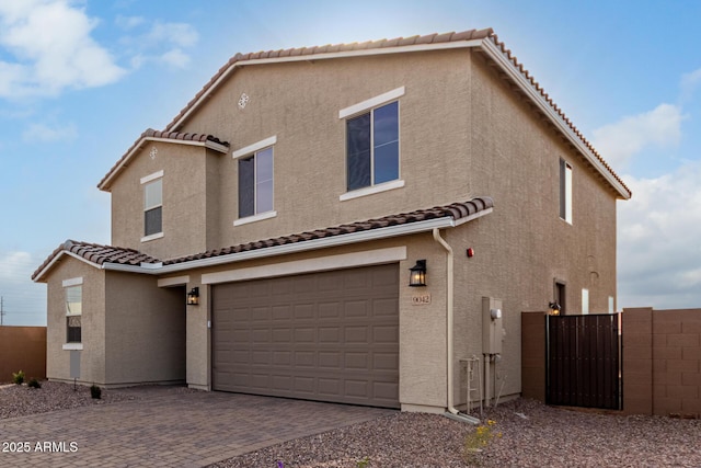 view of front of property featuring a garage, decorative driveway, fence, and stucco siding