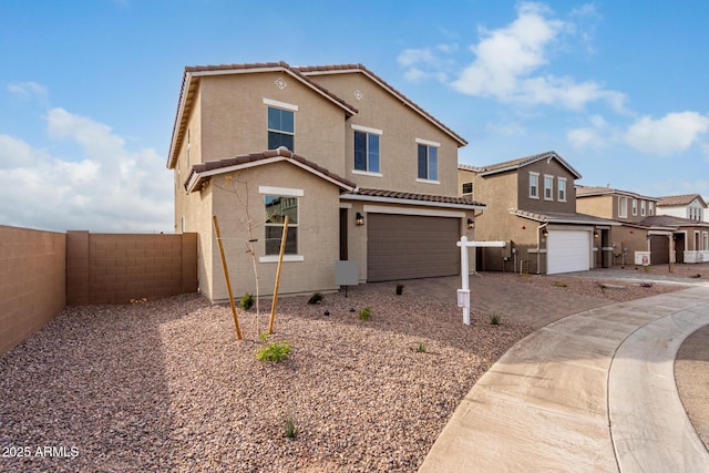 traditional-style home featuring a tile roof, an attached garage, fence, decorative driveway, and stucco siding