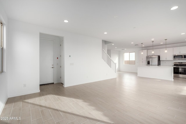 unfurnished living room featuring light wood-style flooring, stairway, baseboards, and recessed lighting