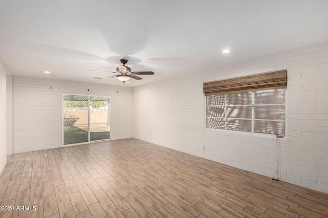 spare room with hardwood / wood-style flooring, ceiling fan, and brick wall