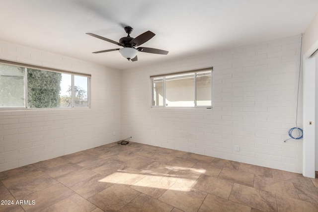 spare room featuring ceiling fan, plenty of natural light, and brick wall