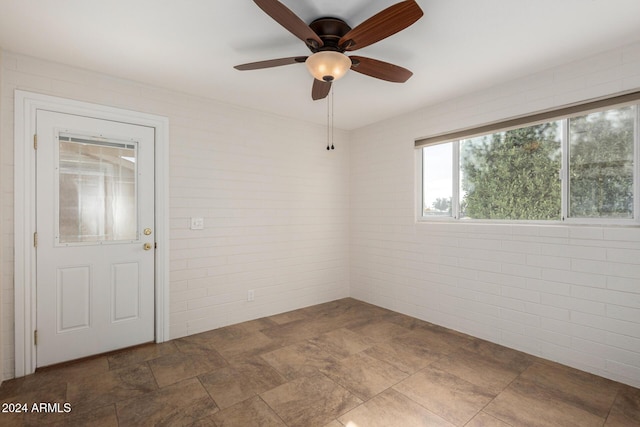 spare room with ceiling fan and brick wall