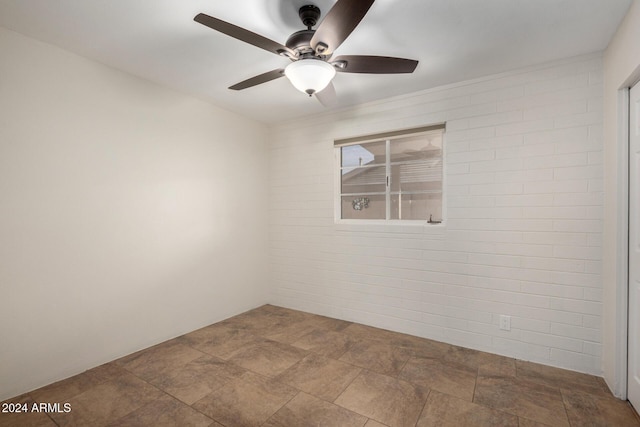 unfurnished room with ceiling fan and brick wall