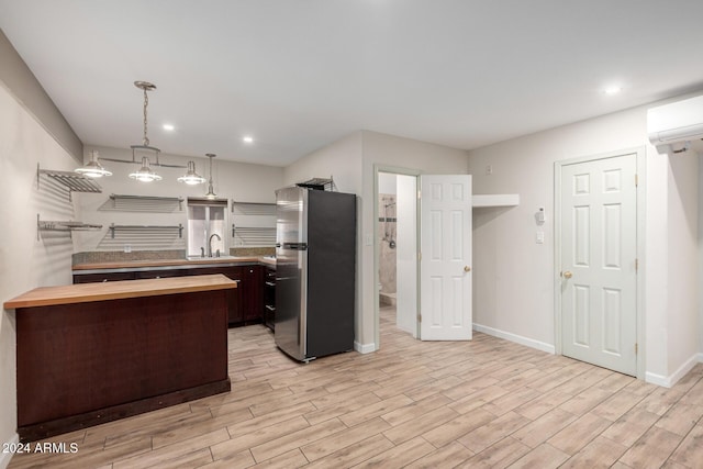 kitchen featuring pendant lighting, sink, stainless steel refrigerator, light hardwood / wood-style floors, and a wall unit AC