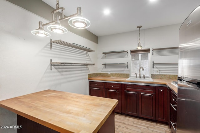 kitchen with sink, hanging light fixtures, light hardwood / wood-style flooring, butcher block countertops, and stainless steel fridge