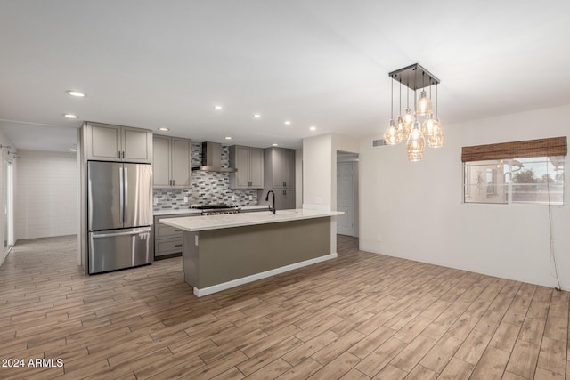 kitchen with gray cabinetry, pendant lighting, light hardwood / wood-style flooring, wall chimney exhaust hood, and appliances with stainless steel finishes