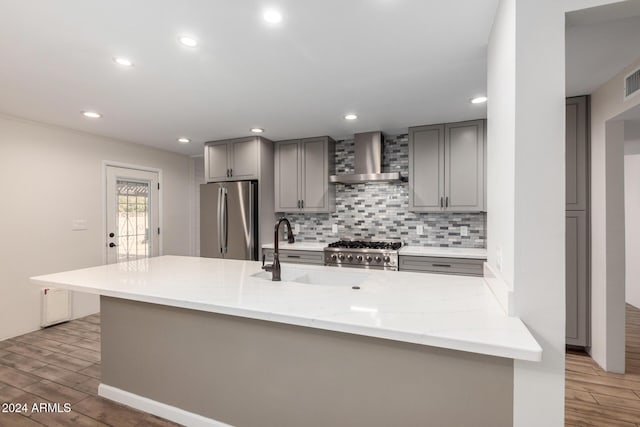 kitchen with wall chimney range hood, sink, light hardwood / wood-style flooring, light stone counters, and stainless steel appliances