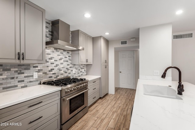 kitchen featuring wall chimney range hood, sink, light hardwood / wood-style flooring, light stone countertops, and high end stove