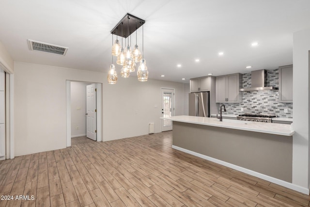 kitchen featuring gray cabinetry, wall chimney range hood, hanging light fixtures, appliances with stainless steel finishes, and light hardwood / wood-style floors