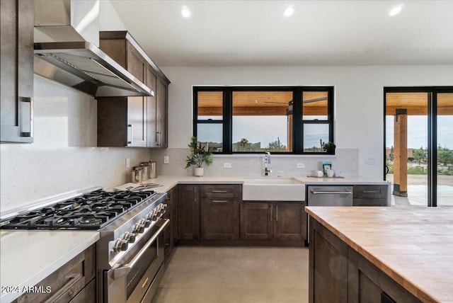 kitchen featuring dark brown cabinetry, sink, backsplash, wall chimney range hood, and stainless steel appliances