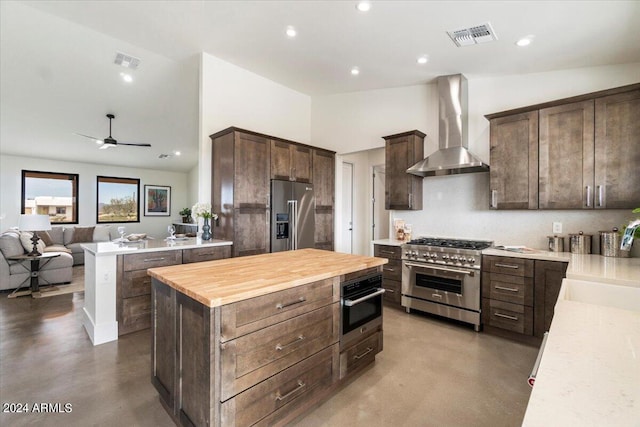 kitchen featuring wooden counters, concrete floors, wall chimney exhaust hood, a center island, and high quality appliances