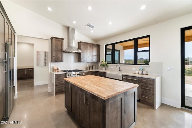 kitchen featuring a center island, wooden counters, sink, wall chimney range hood, and dark brown cabinets