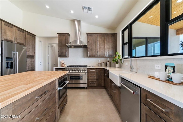 kitchen with sink, dark brown cabinets, wall chimney range hood, high quality appliances, and vaulted ceiling