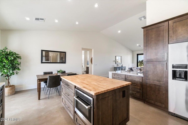 kitchen with a kitchen island, dark brown cabinetry, butcher block counters, white refrigerator with ice dispenser, and vaulted ceiling