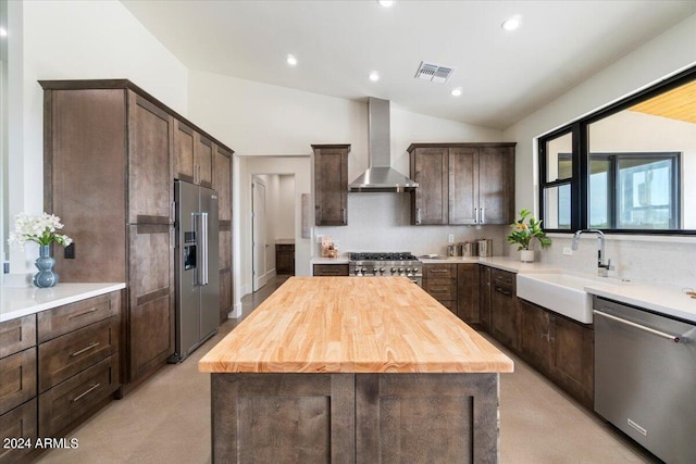 kitchen featuring appliances with stainless steel finishes, wall chimney exhaust hood, vaulted ceiling, and a center island