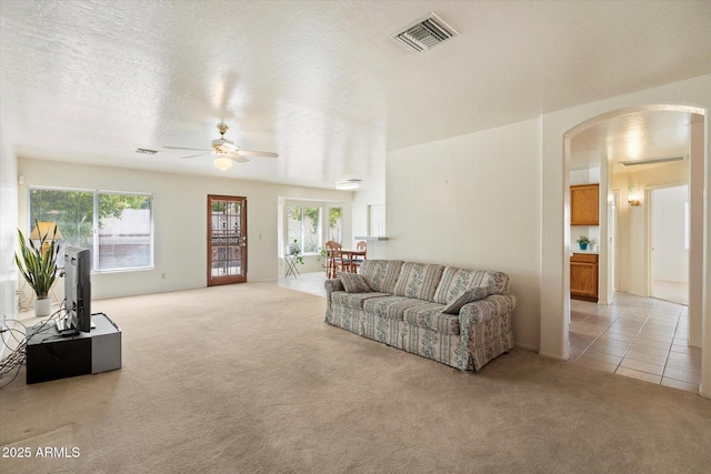 63 W Los Arboles Dr, Tempe, AZ 85284 - living room featuring ceiling fan, arched walkways, light colored carpet, visible vents, and a healthy amount of sunlight
