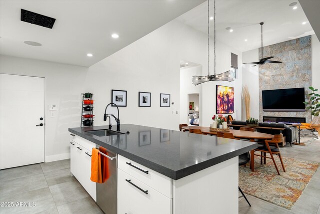 kitchen featuring stainless steel dishwasher, sink, a center island with sink, white cabinets, and hanging light fixtures