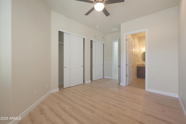 unfurnished bedroom featuring baseboards, two closets, ensuite bathroom, and light wood-style floors