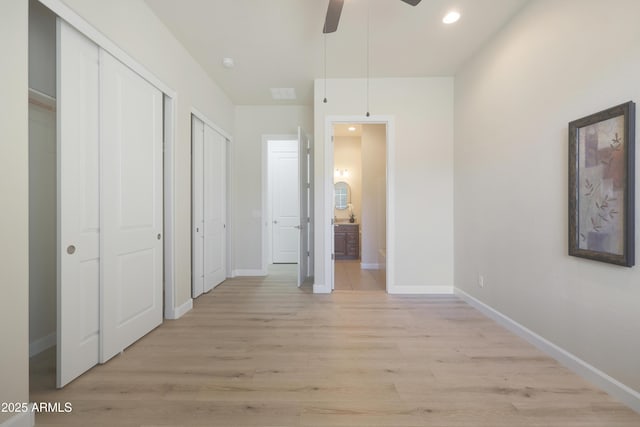 unfurnished bedroom with connected bathroom, multiple closets, light wood-style floors, and baseboards