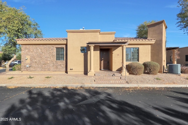 view of front of property with a tile roof, central air condition unit, stone siding, and stucco siding