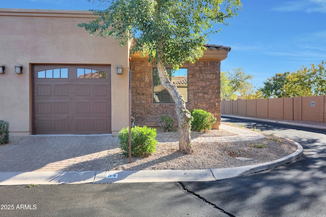 view of front of property with a garage, fence, stone siding, and stucco siding