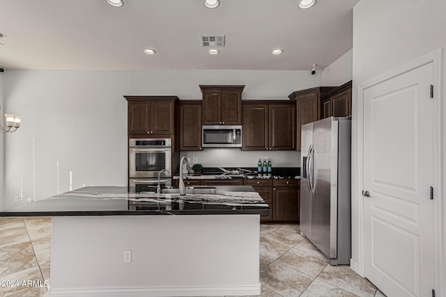 kitchen featuring stainless steel appliances, dark countertops, recessed lighting, visible vents, and an island with sink