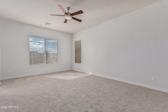 spare room with light carpet, ceiling fan, visible vents, and baseboards