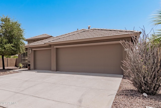 view of front of house featuring an attached garage, fence, driveway, a tiled roof, and stucco siding