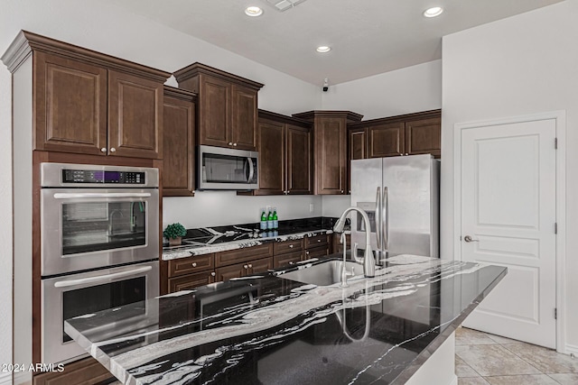 kitchen with sink, light tile patterned floors, dark brown cabinets, stainless steel appliances, and a center island with sink