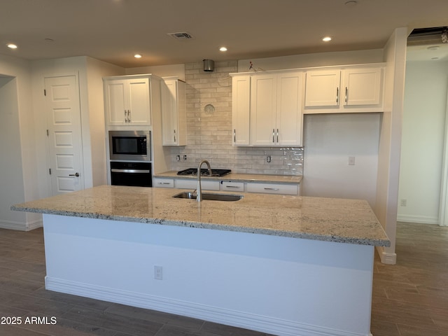 kitchen featuring light stone countertops, white cabinets, stainless steel appliances, backsplash, and a center island with sink