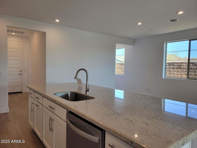 kitchen with light stone countertops, dishwasher, white cabinetry, sink, and a kitchen island with sink