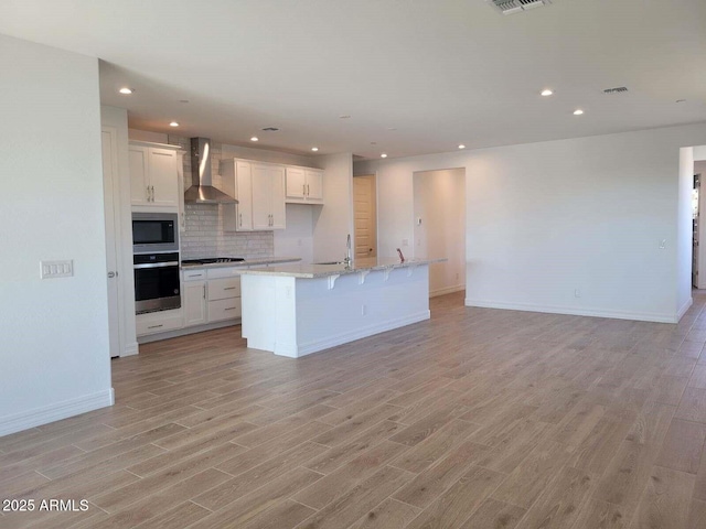 kitchen featuring appliances with stainless steel finishes, an island with sink, white cabinets, and wall chimney range hood