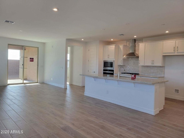 kitchen with white cabinetry, wall chimney exhaust hood, stainless steel appliances, and a kitchen island with sink