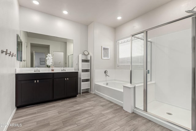 bathroom featuring double vanity, a shower stall, a bath, a sink, and wood finished floors