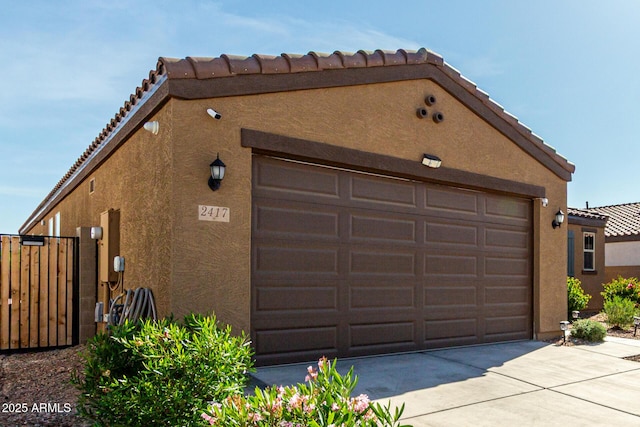 exterior space with a garage, a tile roof, fence, concrete driveway, and stucco siding