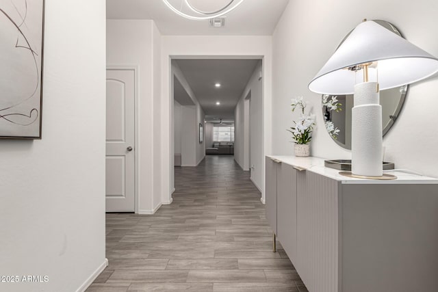 hallway featuring light wood-style floors, baseboards, and visible vents