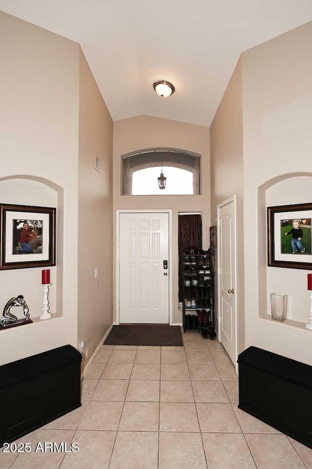 entrance foyer featuring baseboards, light tile patterned floors, and high vaulted ceiling