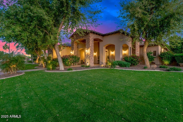 mediterranean / spanish-style home featuring stone siding, stucco siding, a tile roof, and a yard