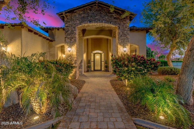 doorway to property with a tiled roof, stone siding, and stucco siding