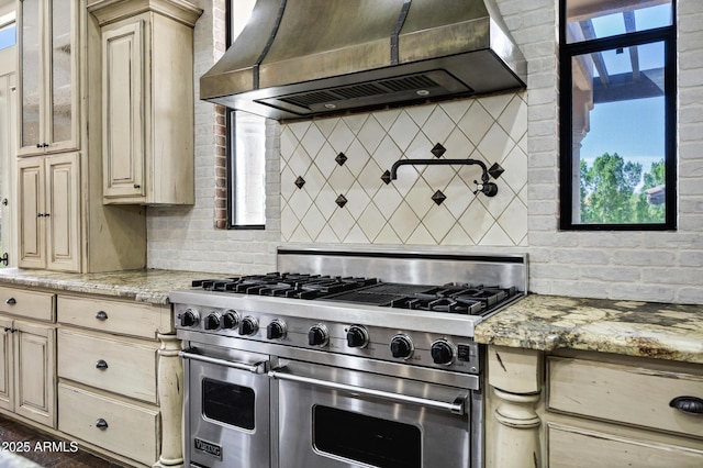 2300 E Sanoque Ct, Gilbert, AZ 85298 - kitchen with range with two ovens, wall chimney exhaust hood, backsplash, cream cabinets, and light stone countertops