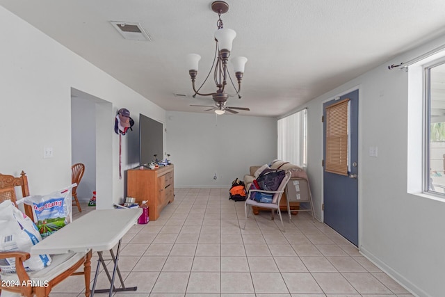 interior space featuring light tile patterned floors, ceiling fan with notable chandelier, visible vents, and baseboards